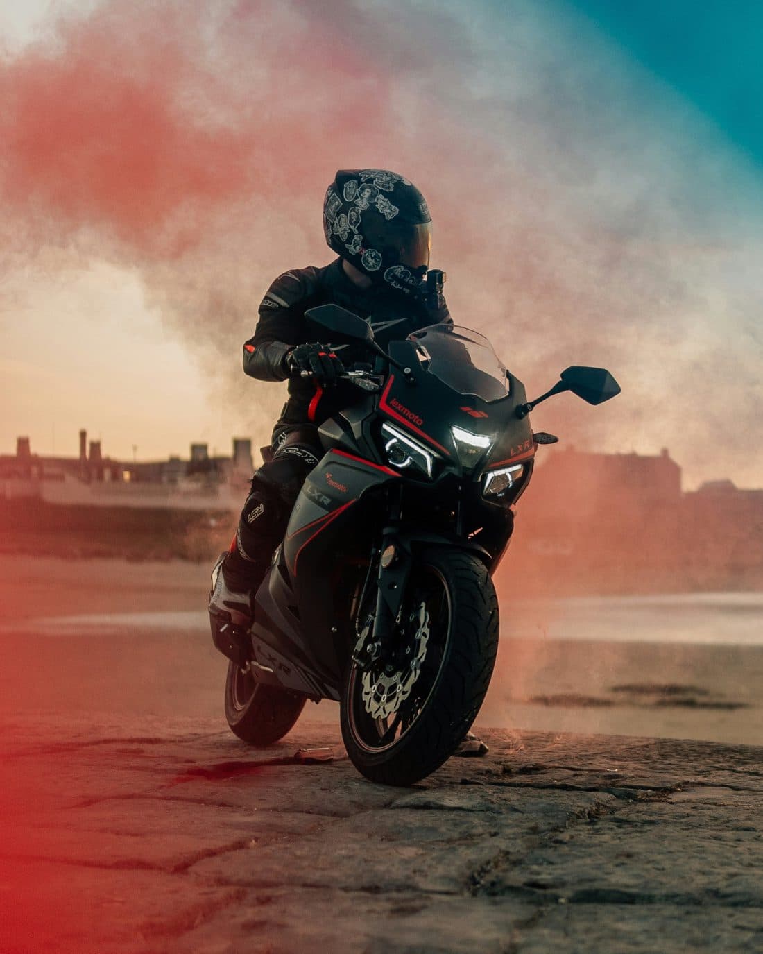 A rider in black leathers on a sport bike, coloured smoke drifting behind